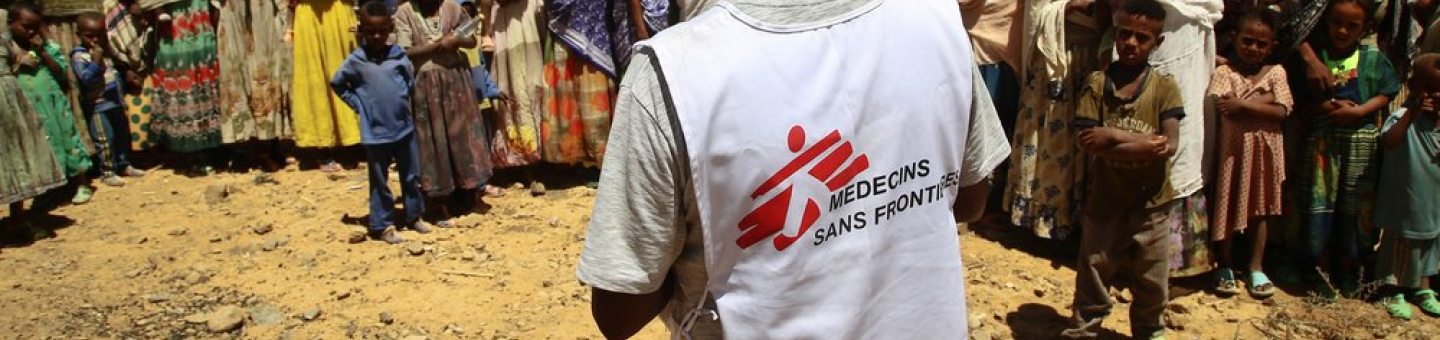 Ein Übersetzer von Ärzte ohne Grenzen vor einer Gruppe von Frauen und Kindern, die auf eine Behandlung durch Ärzte ohne Grenzen in einem Dorf in Tigray warten. Patientinnen einer mobilen Klinik in Tigray
