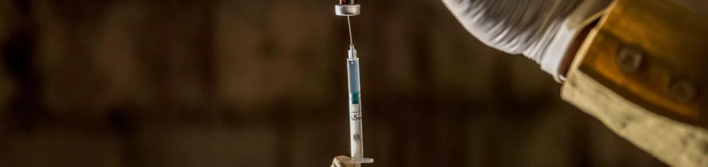 Zwei Hände die Impfstoff in eine Spritze ziehen