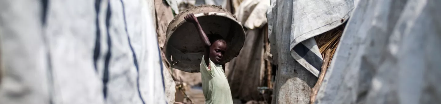 Ein Mädchen hält einen großen Korb über ihren Kopf, während sie zwischen mehreren Zelten steht