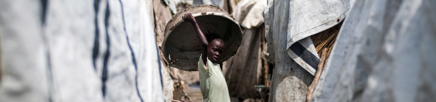 Die Lebensbedingungen in Vertriebenenlagern im Südsudan, wie hier in Malakal, sind prekär. Ein Mädchen hält einen großen Korb über ihren Kopf, während sie zwischen mehreren Zelten steht