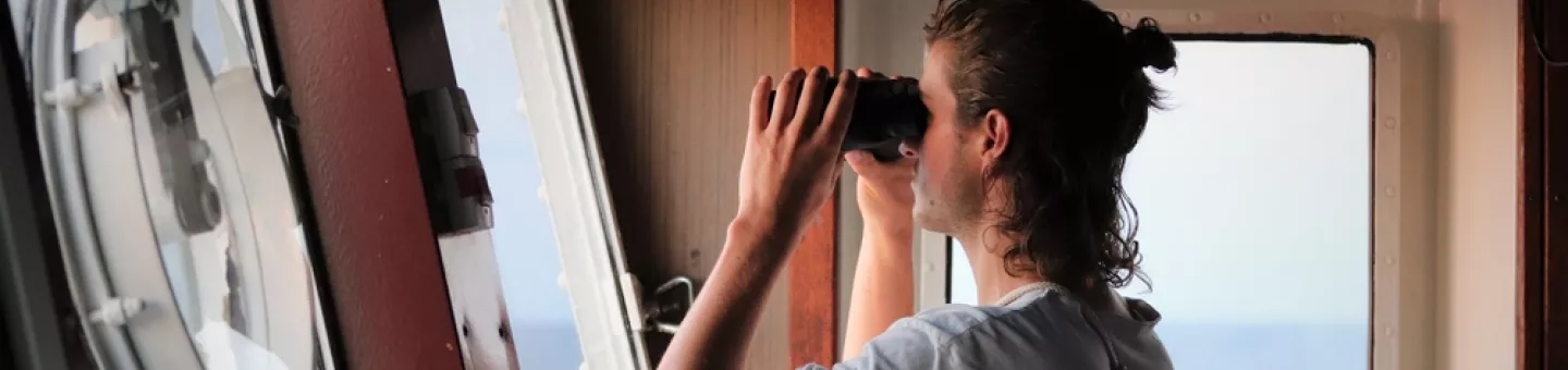 Ein Mitarbeiter von Ärzte ohne Grenzen steht auf einer Schiffsbrücke und schaut durch ein Fernglas.