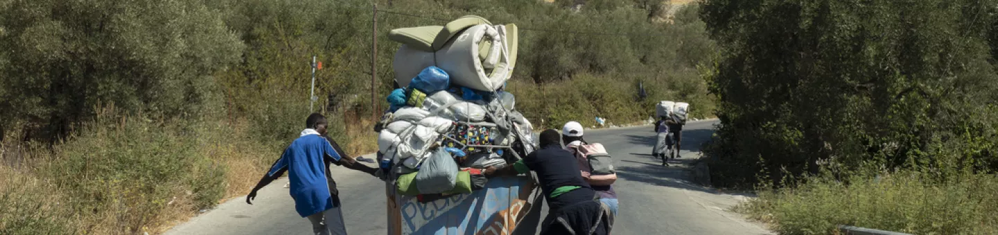 Geflüchtete laufen auf einer Straße, in ihrer Mitte ein Wagen mit Ihrem Hab und Gut.