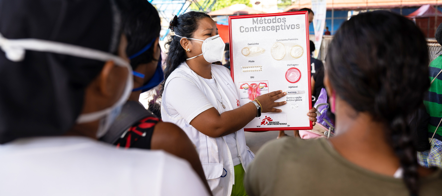 Venezolanische Migrant*innen und Geflüchtete in Nordbrasilien Eine Frau mit Maske spricht vor Anderen, ein Plakat zu Kontrazeptiva in der Hand