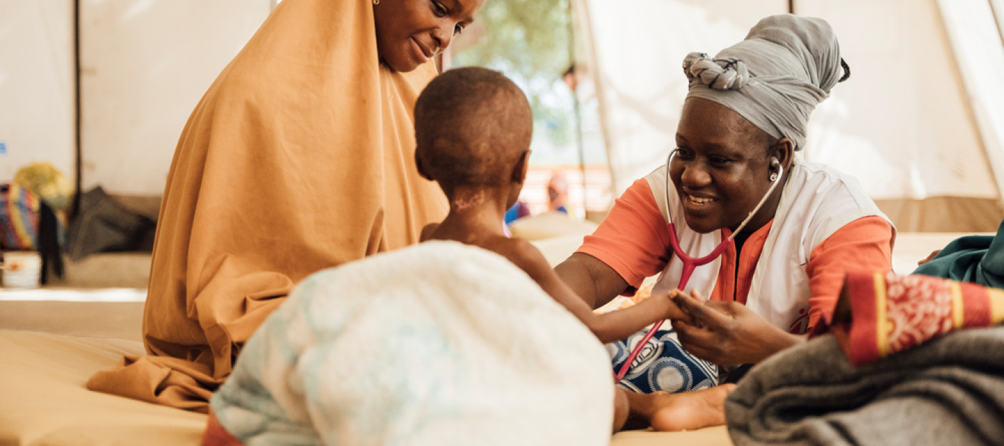Unsere Ärztin Faïza Ouedraogo hat den zweijährigen Edriss während ihrem Einsatz in Niger behandelt. Spenden: Ärztin hört Kleinkind mit Stethoskop ab, daneben Mutter