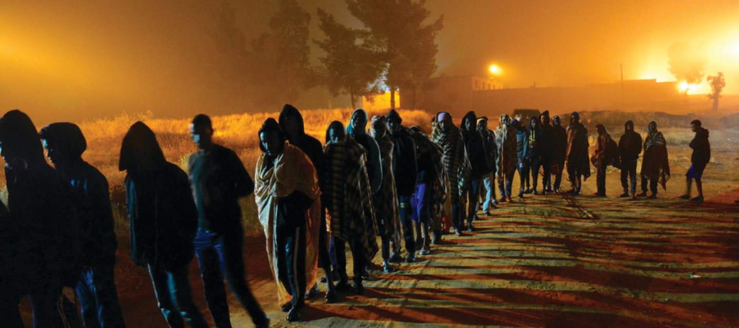 Geflüchtete und Migrant*innen in den Internierungslagern Zintan und Gharyan in Libyen Zahlreiche Menschen stehen in der Dämmerung in einer langen Schlange