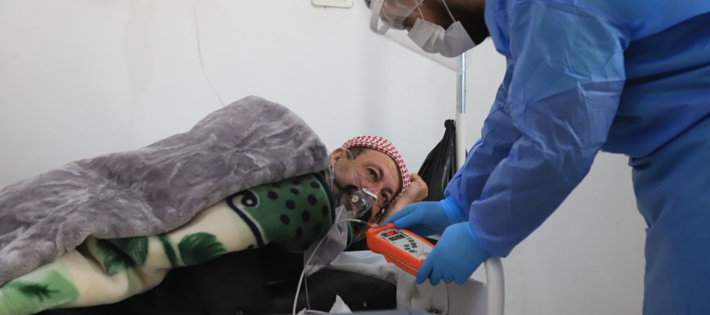 Nordsyrien: Die Zahlen von Covid-19-Patient*innen steigen stark an Ein Mann in blauem Schutzanzug beugt sich zu einem Mann herunter, der künstlich beatmet wird