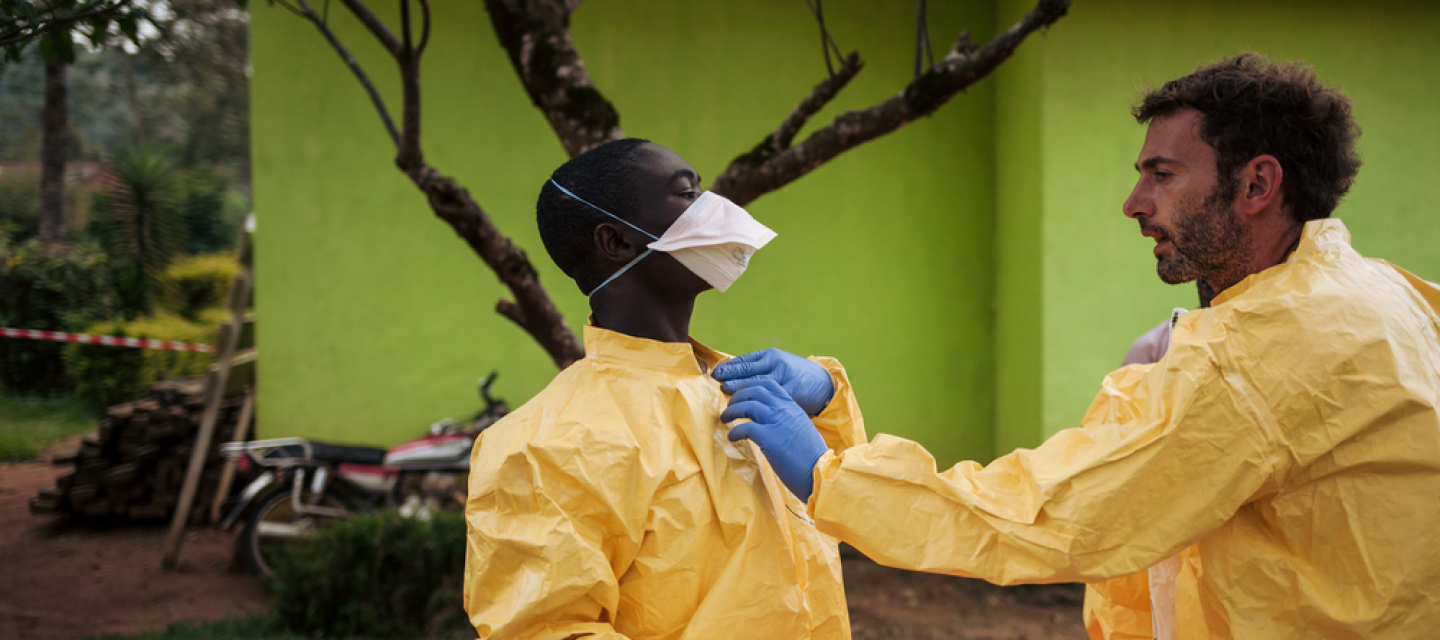 Unser Hygienespezialist Luca Fontana erklärt einem Kollegen in Kalunguta, D.R. Kongo, wie sich die Ebola-Gesundheitsteams gegen das Virus schützen können. Hygienespezialist hilft Kollege in Schutzkleidung