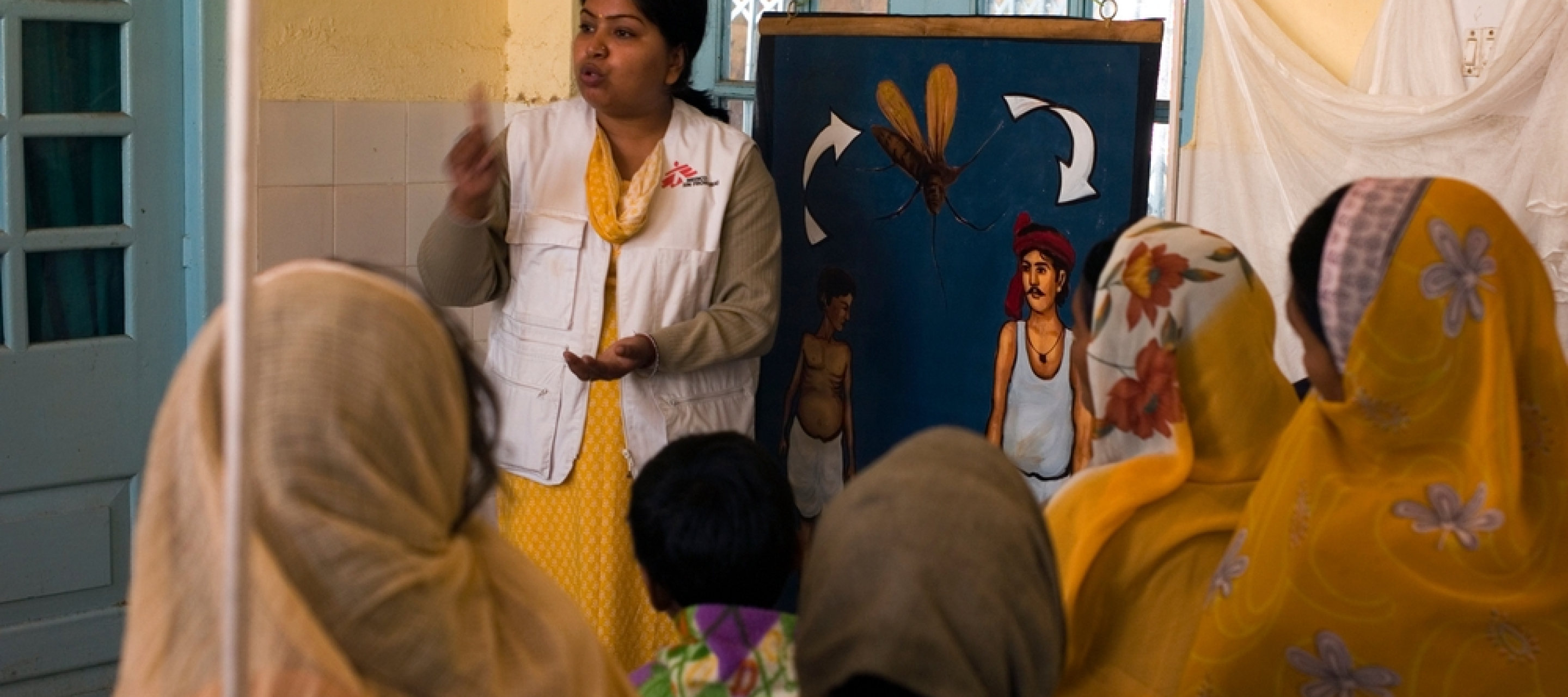 Eine Lehrerin erteilt ihren Schülerinnen Präventionsunterricht zu Kala Azar und  Malaria