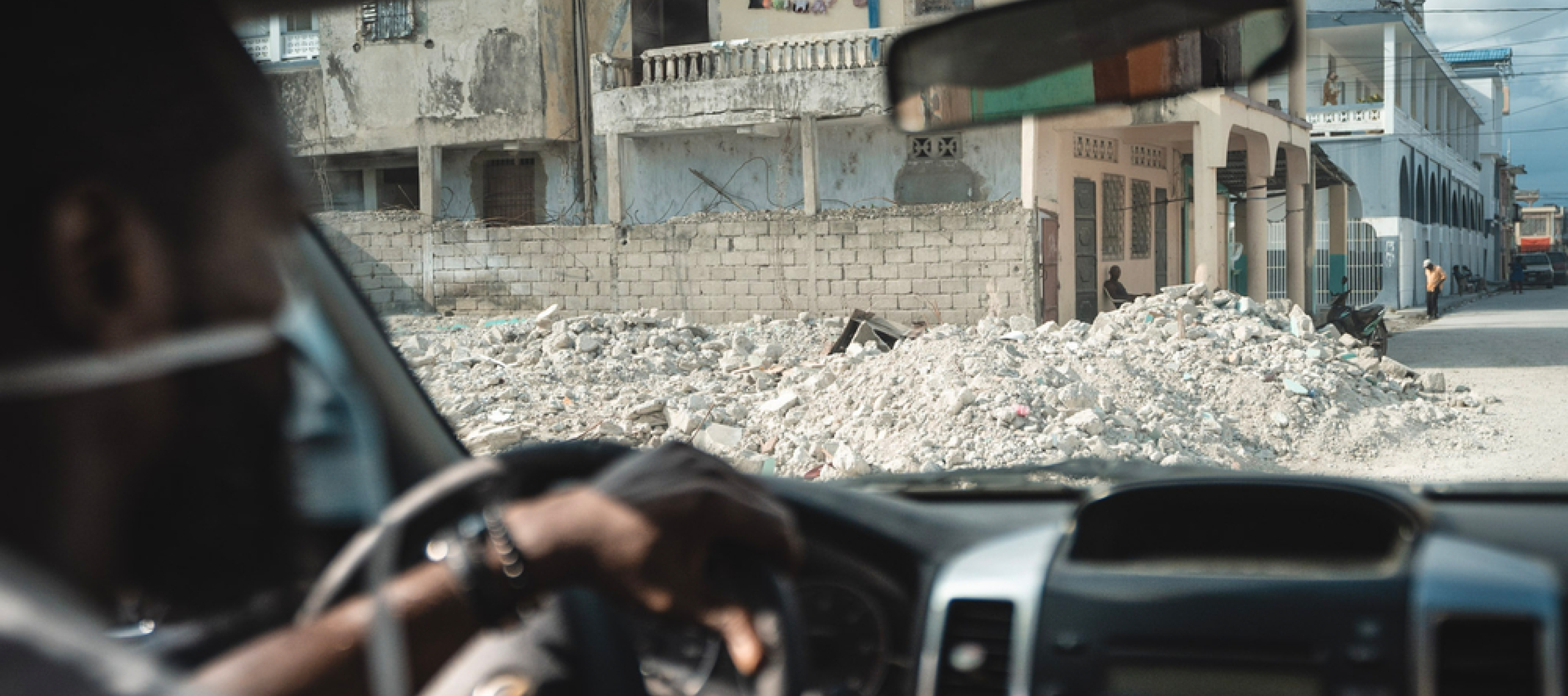 One of our employees is sitting in a car. In the background, there is visible destruction due to an earthquake.