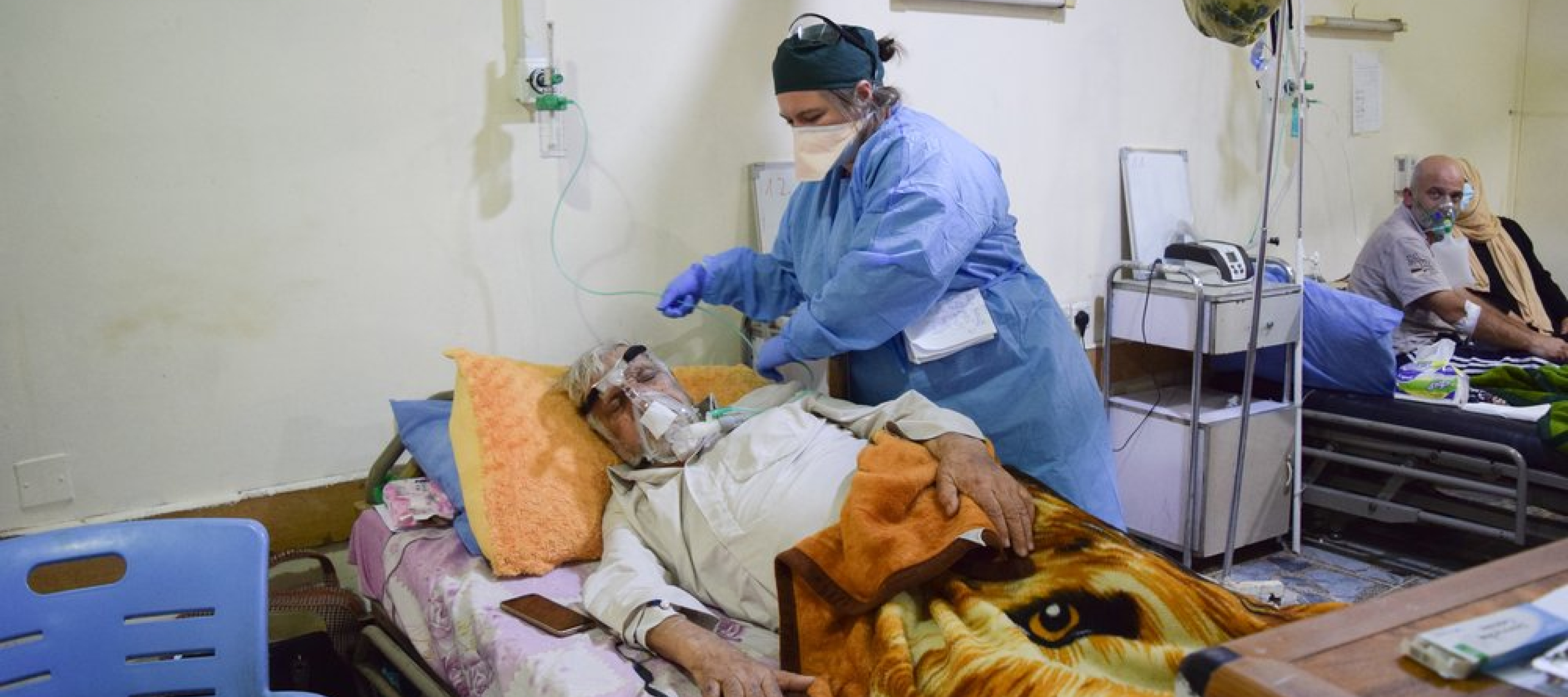 Ein Patient in einem Krankenhausbett mit Sauerstoffmaske, neben ihm eine Person des Pflegepersonals