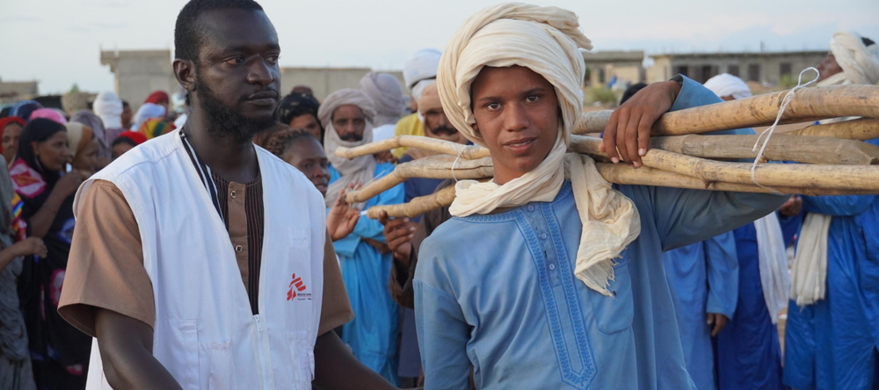 Ein junger Mann mit Material für eine Notunterkunft und ein Mitarbeiter von Ärzte ohne Grenzen in Mali.