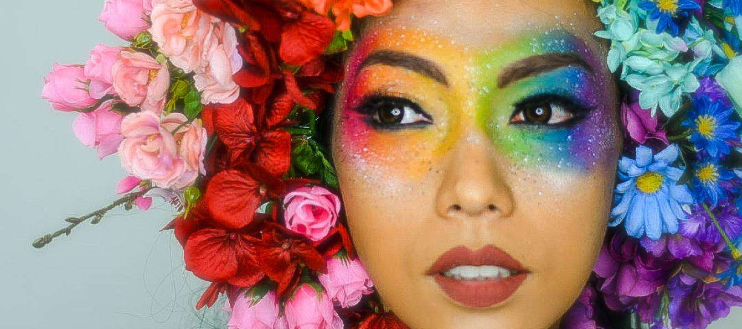 Frau mit regenbogenfarbenem Blumenkranz und Augenmakeup.