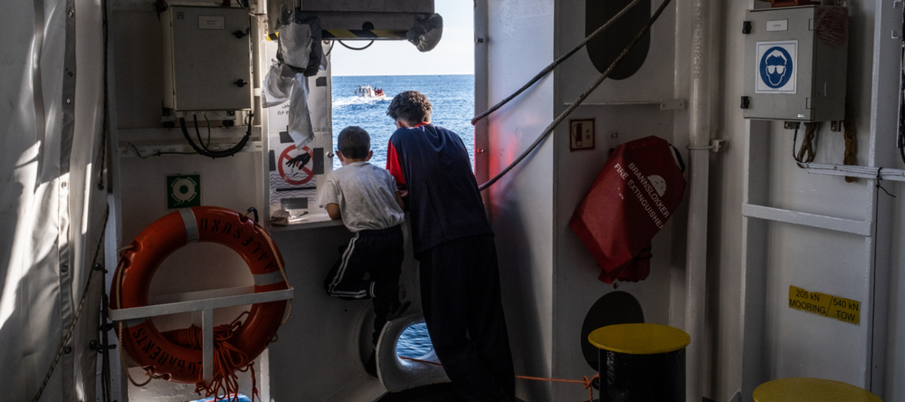 Zwei Jungen stehen am Fenster eines Schiffes und schauen auf das Meer.