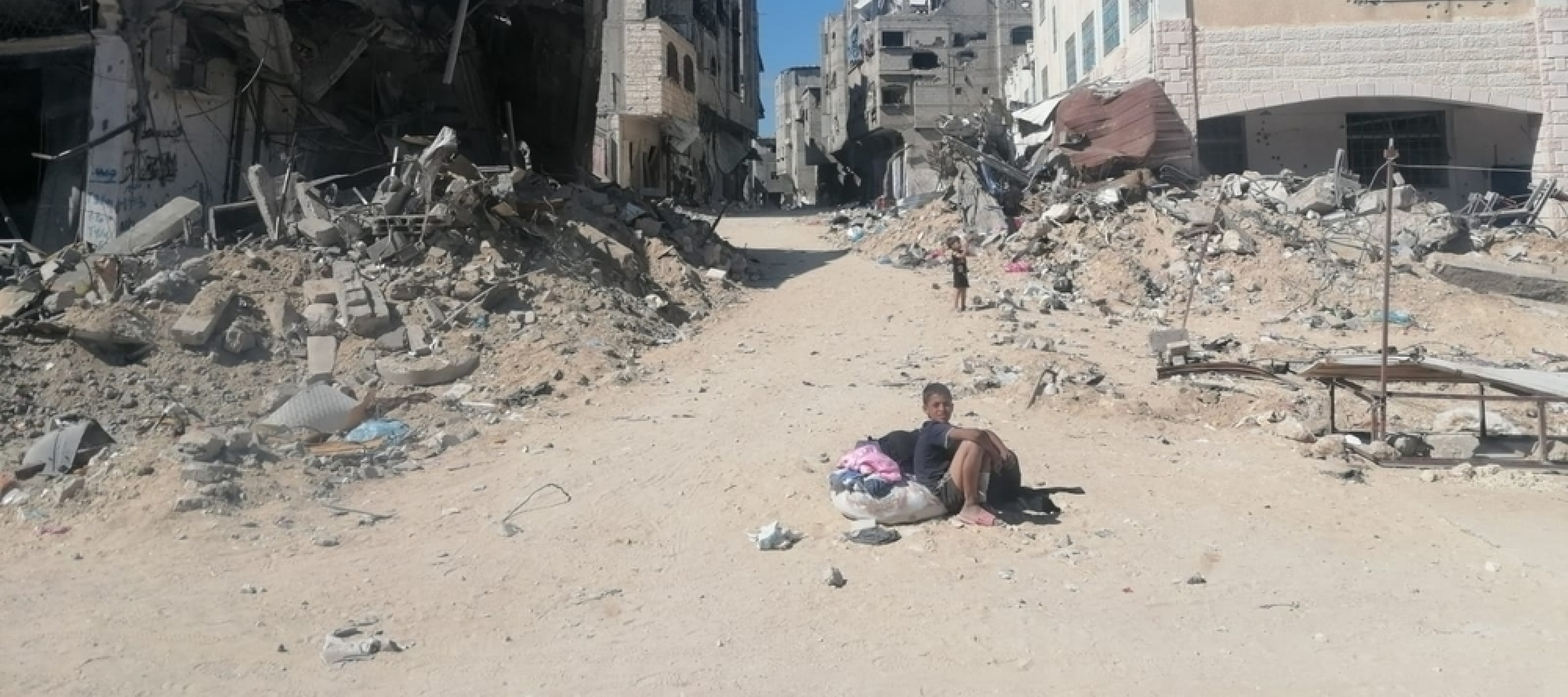 Wir bieten Angebote zu psychische Gesundheit im Gazastreifen. Junge sitzt auf Sandstraße in zerstörter Stadt