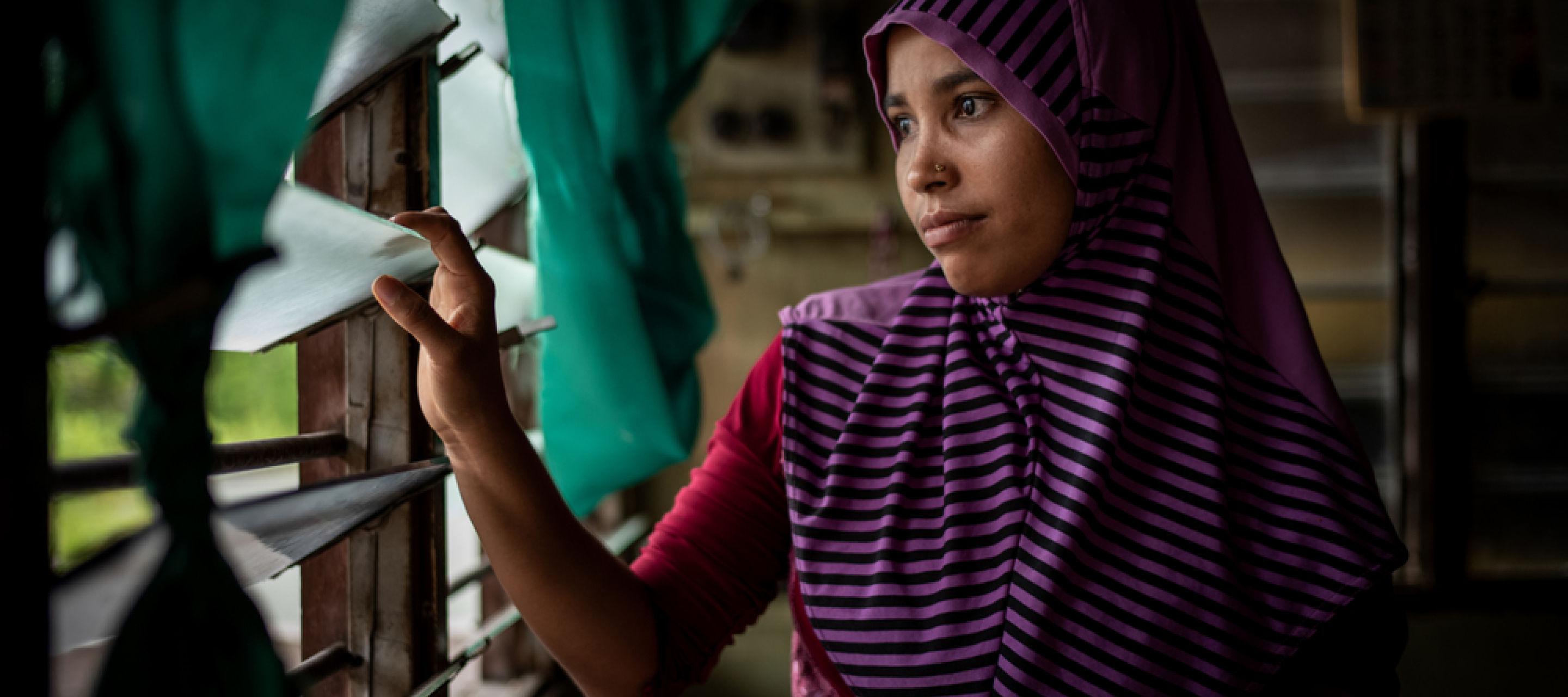 Die gefährliche Fluchtroute vieler Rohingya endet in Malaysia. Eine Frau sitzt im Dunkeln und blickt durch vergitterte Fenster