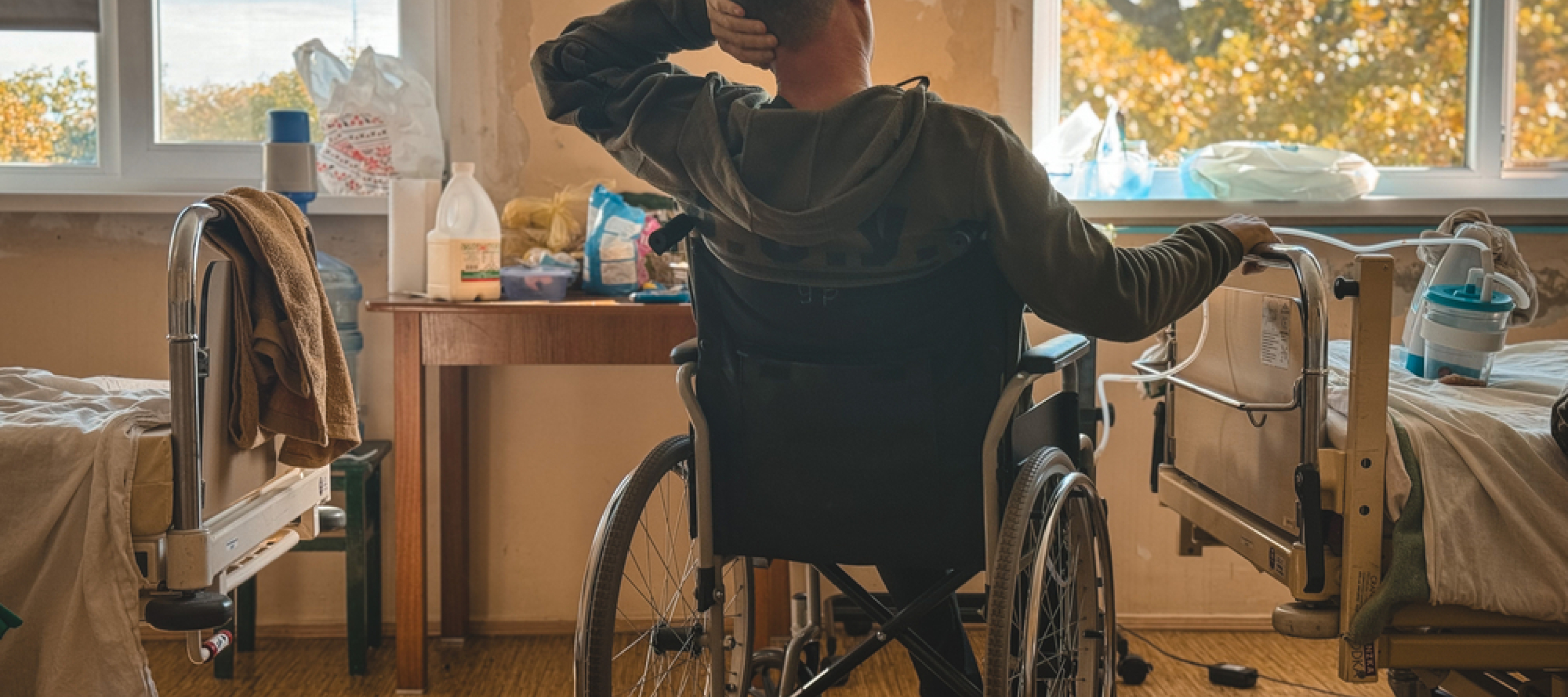 Patient sitzt nach Kriegsverletzungen im Rollstuhl und lernt in unserem Rehabilitationsprojekt wieder zu gehen. Patient sitzt im Rollstuhl in einem Krankenhauszimmer