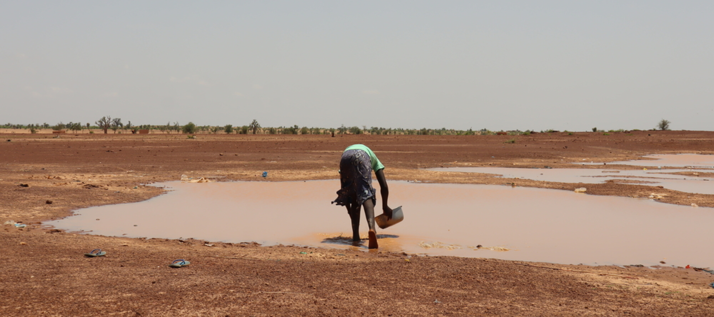 Eine Person in Burkina Faso schöpft Regenwasser vom Boden. Person schöpft Regenwasser vom Boden