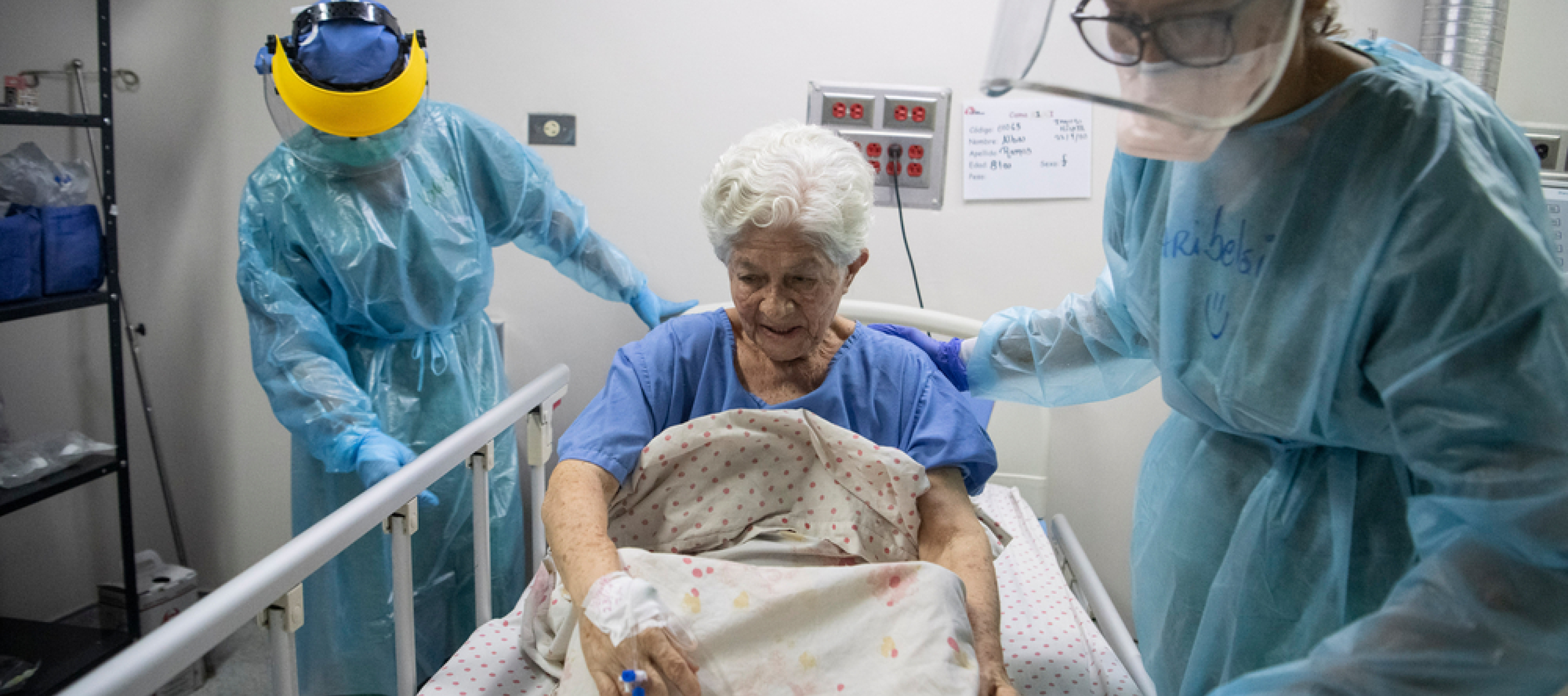 Alte Frau wird von zwei Pflegern in Schutzkleidung betreut