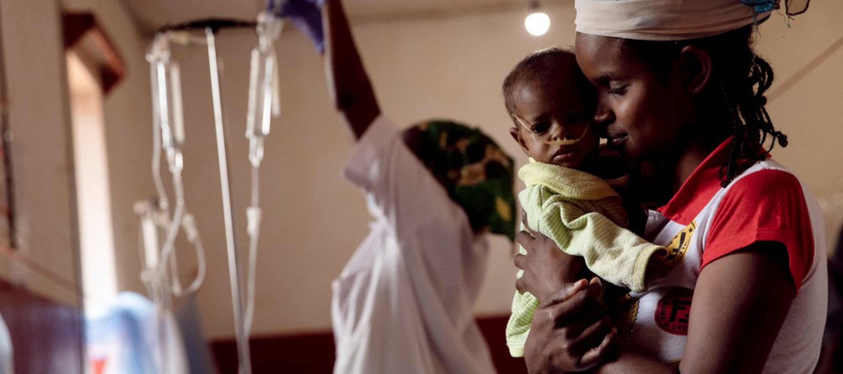 Zentralafrikanische Republik: Mutter hält ihr krankes Kind im Arm. Im Hintergrund ein Mitarbeiterin und Infusionen