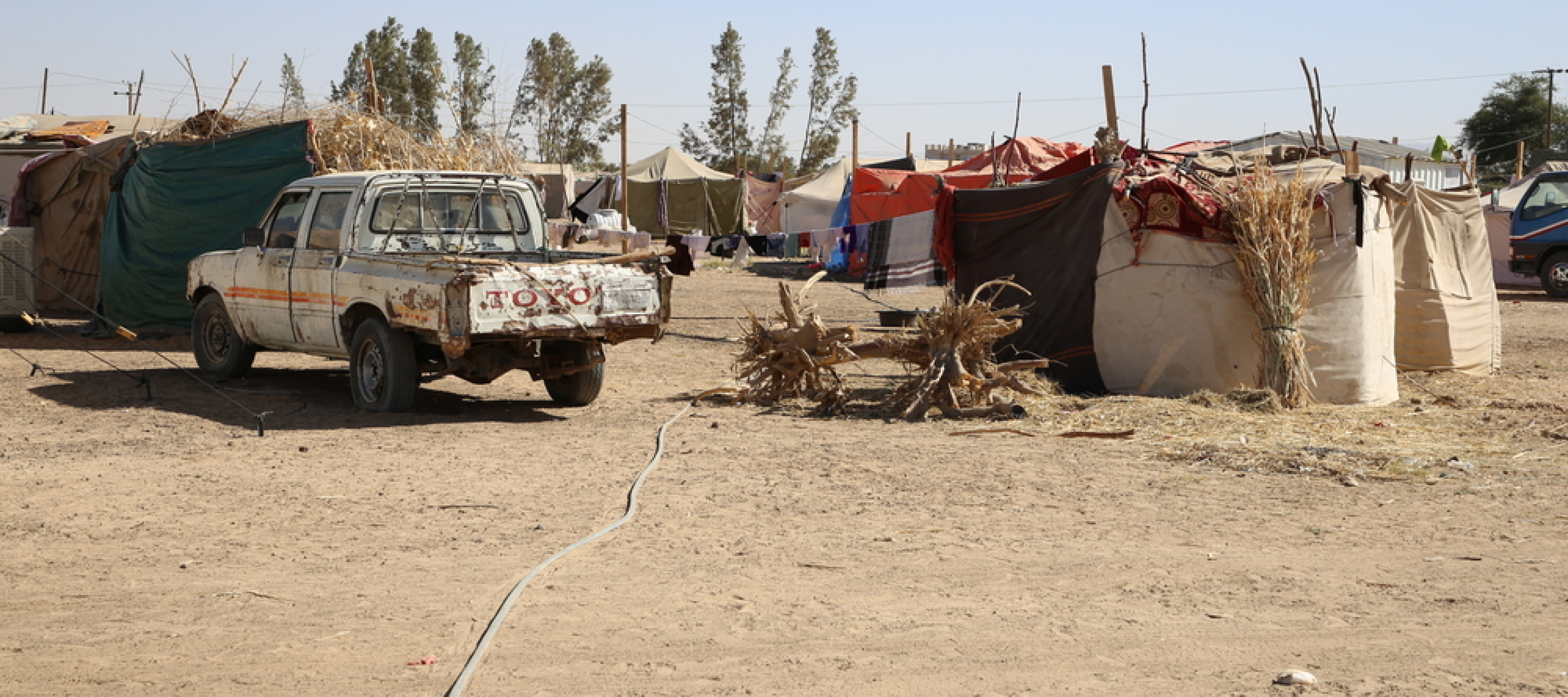 Ein altes Auto vor einem Camp mit vielen Zelten in einer wüstenähnlichen Landschaft