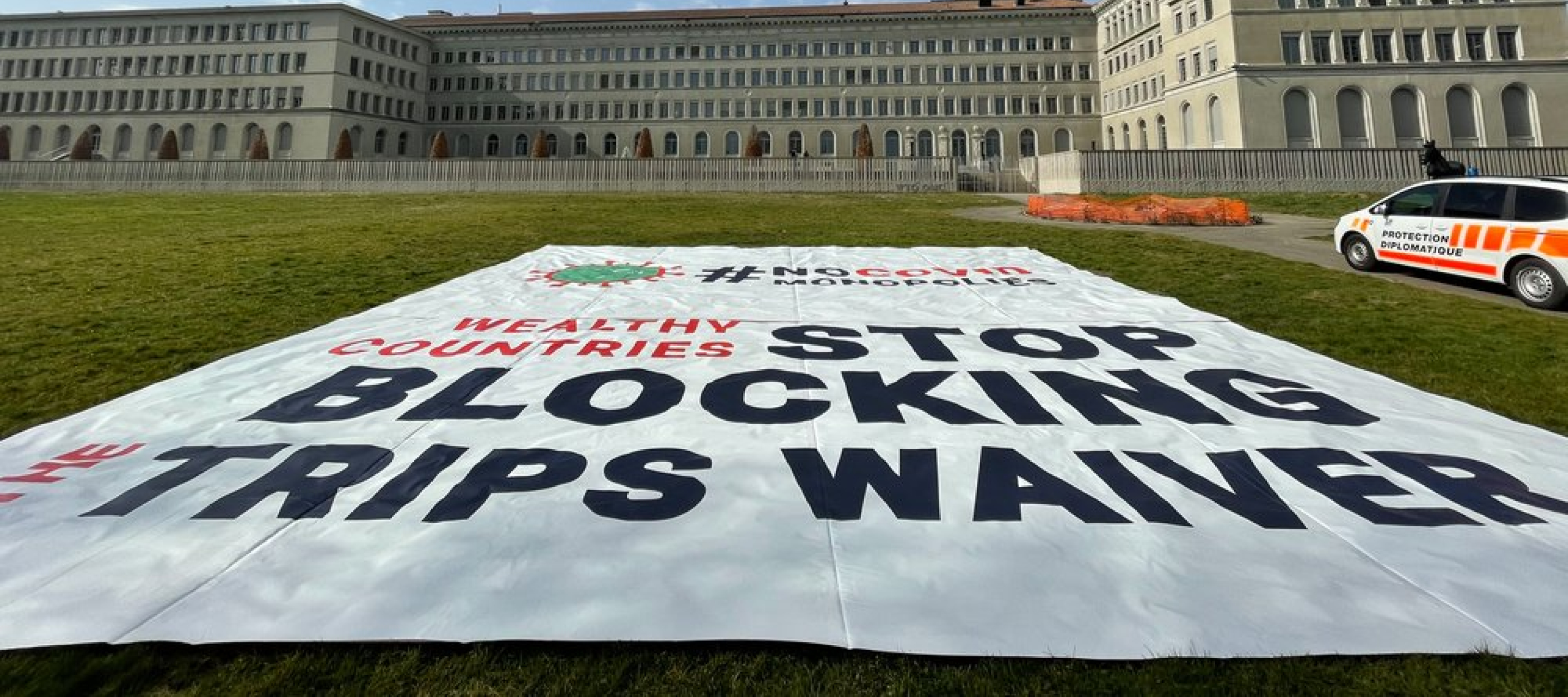 Die Aufforderung zur Unterstützung des TRIPS-Waiver direkt vor dem Gebäude der WTO Das Gebäude der WTO und das Plakat zum TRIPS-Waiver