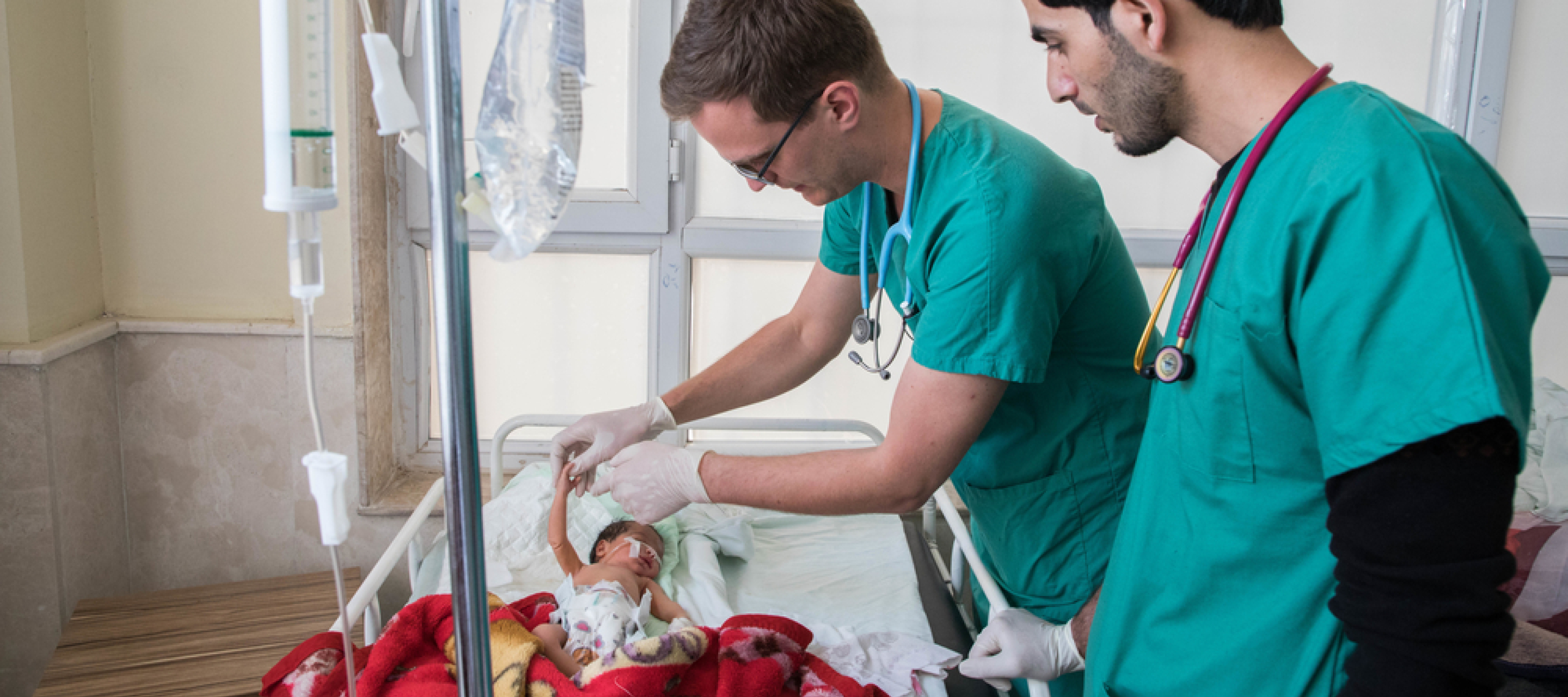 Zwei Mitarbeiter kümmern sich um ein Neugeborenes in einem Bett