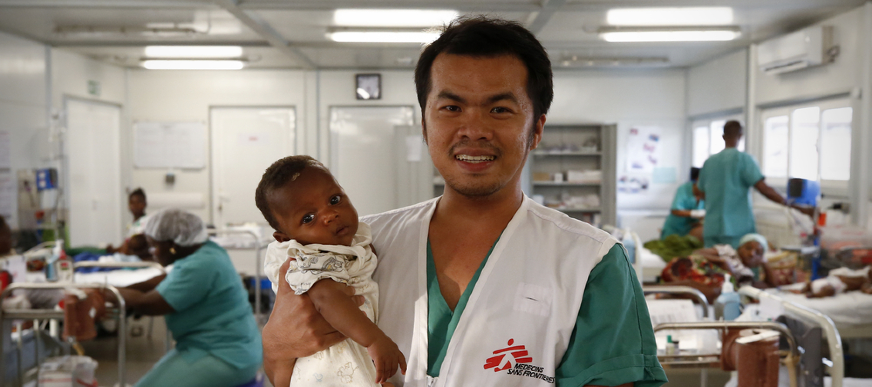 Jerwin Capuras arbeitet als Krankenpfleger auf der Intensivstation unseres Kinderkrankenhauses in Kenema, Sierra Leone. Die meisten jungen Patient*innen werden wegen Malaria, Lungenentzündung, hohem Fieber und Infektionen der Atemwege und des Magen-Darm-Trakts behandelt. Krankenpfleger hält Baby auf dem Arm