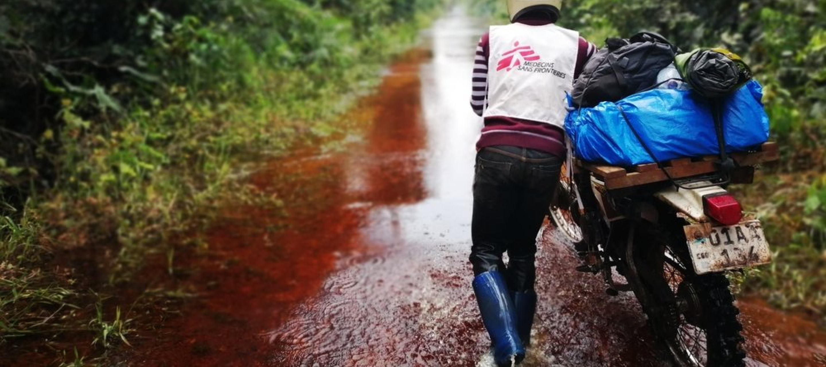 Mitarbeiter mit Motorrad auf überfluteter Straße in der Demokratischen Republik Kongo. Jetzt für den Newsletter anmelden und mehr über die weltweite Nothilfe von Ärzte ohne Grenzen erfahren, wir zum Beispiel über Impfungen gegen Masern in der Demokratischen Republik Kongo.