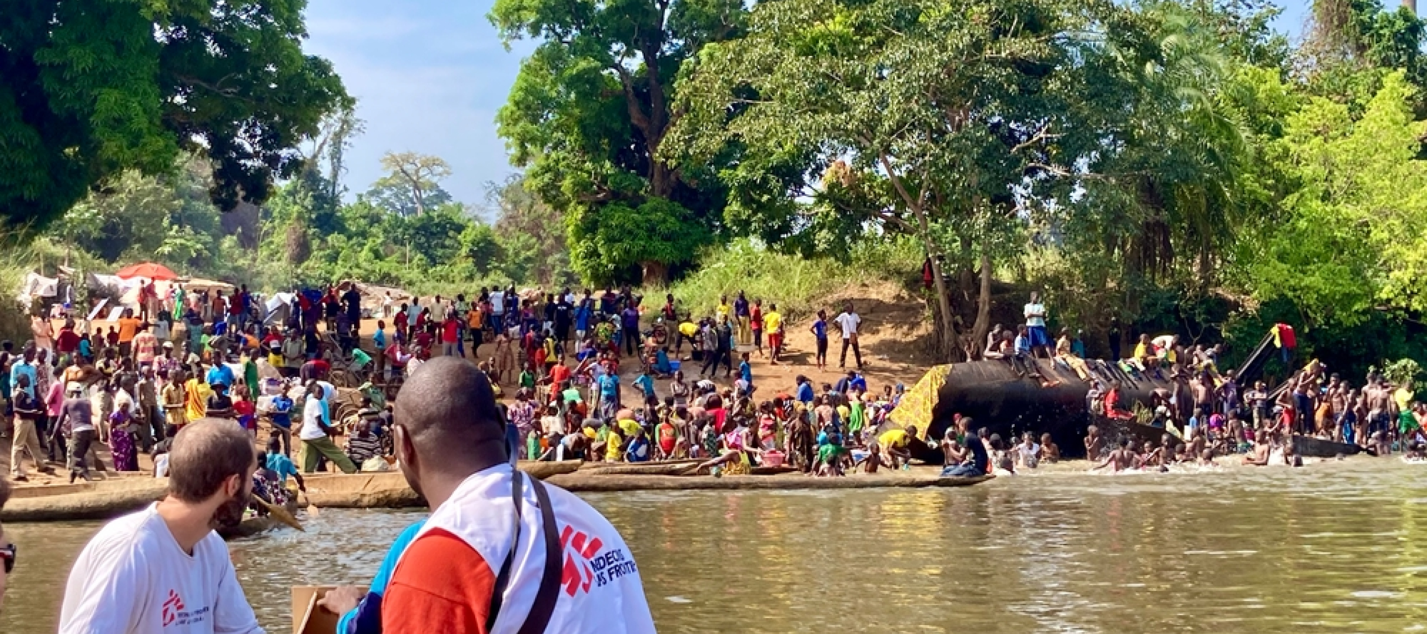 Zwei Männer auf Boot fahren ans Ufer zu Menschengruppe