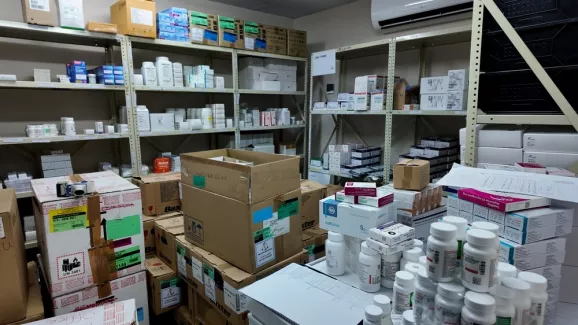 Lagerraum einer Klinik-Apotheke mit Regalen voller Medikamentenschachteln und Kartons sowie Arbeitsfläche mit Arzneiflaschen.