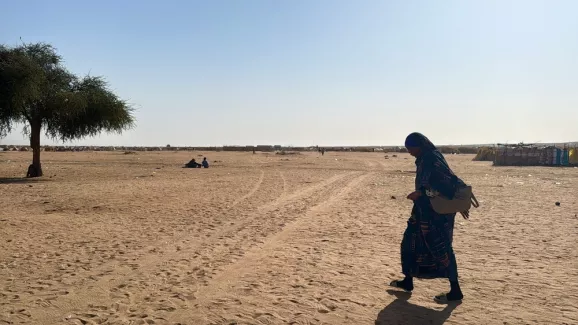 Eine Frau geht alleine über eine freie sandige Fläche.