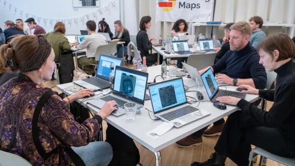 Menschen sitzen an Tischen und kartieren am Laptop