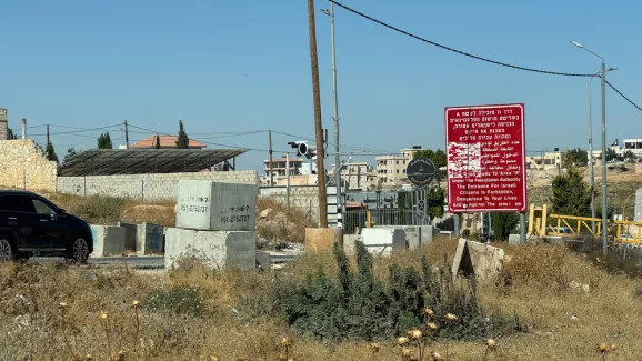 Mehrere Betonblöcke versperren eine Straße neben einem roten Warnschild; im Hintergrund stehen Häuser.