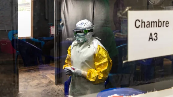 Eine Person trägt Schutzkleidung hinter einer Scheibe