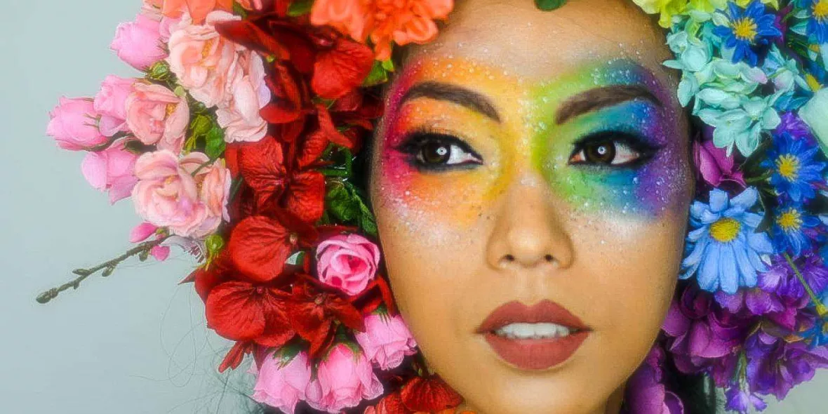 Frau mit regenbogenfarbenem Blumenkranz und Augenmakeup.