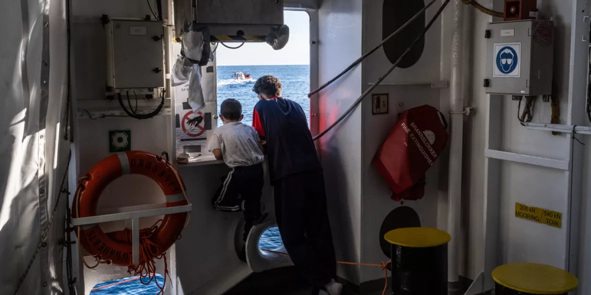 Zwei Jungen stehen am Fenster eines Schiffes und schauen auf das Meer.
