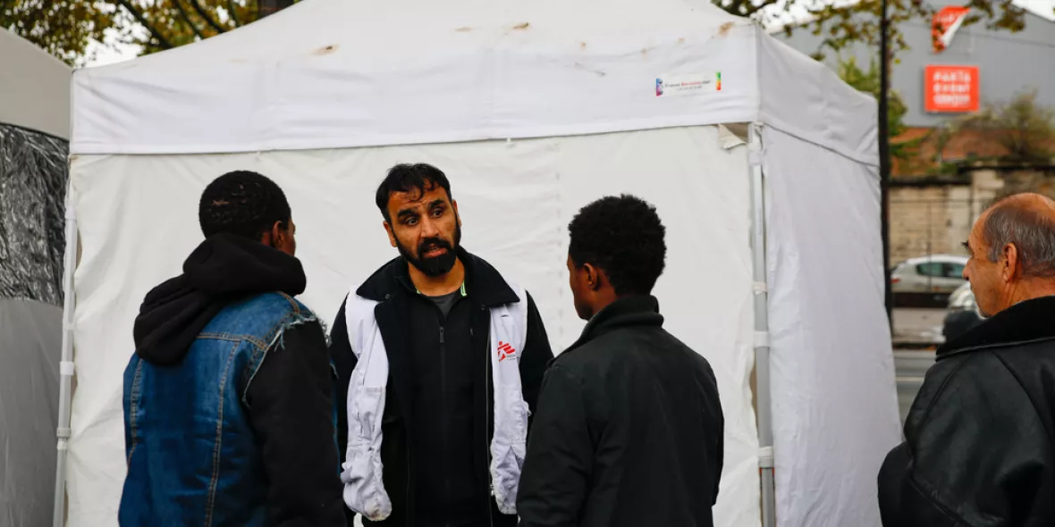 Migranten und ein Mitarbeiter vor einer mobilen Klinik in Calais