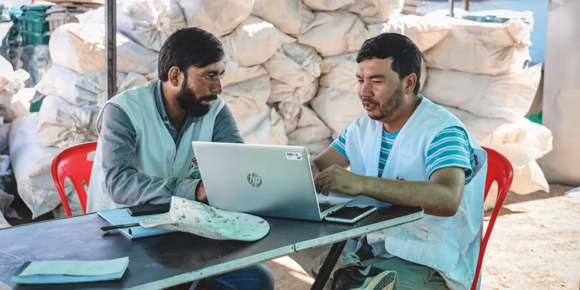FAQ Spenden: Zwei Mitarbeitende sitzen an Tisch und besprechen sich vor Laptop.