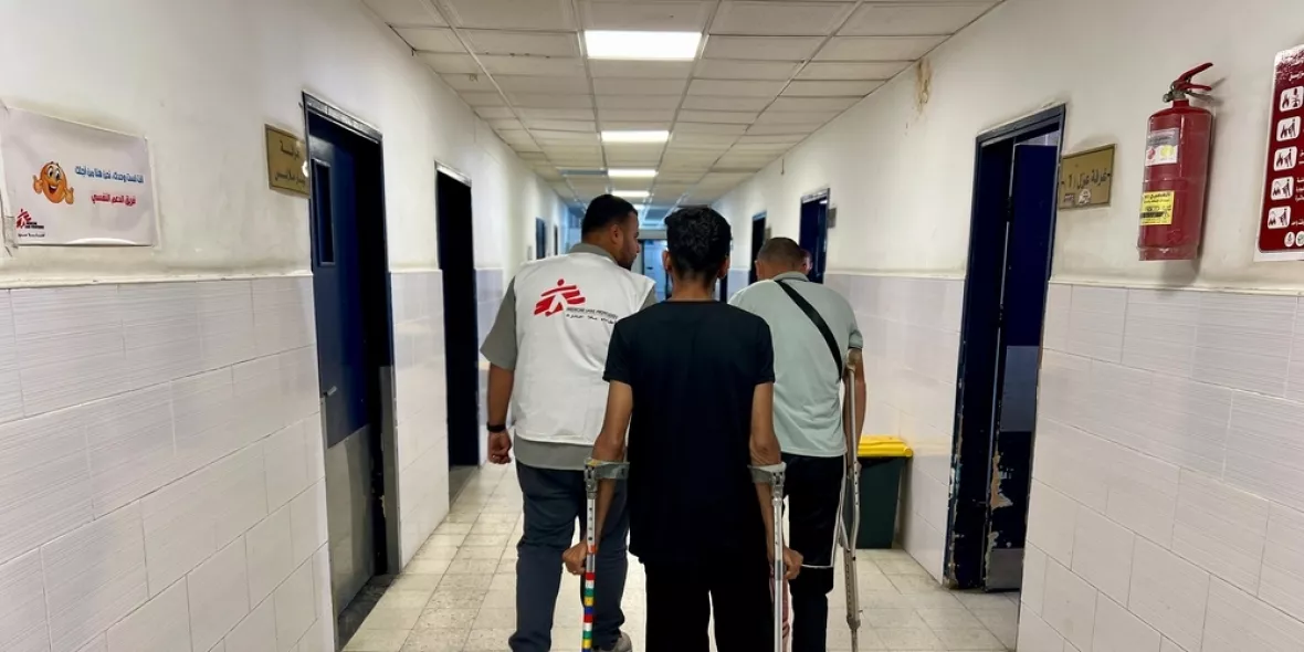 Mitarbeitende und Patient auf Krücken in Krankenhausgang