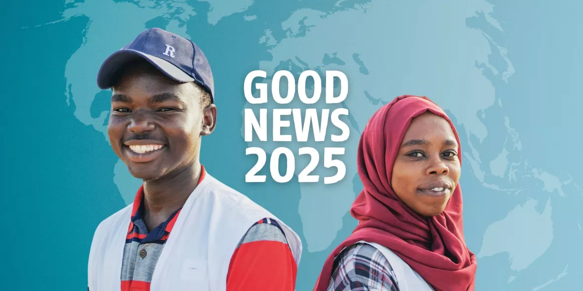 Zwei Personen stehen Rücken an Rücken und lächeln in die Kamera. Dahinter der Schriftzug "Good News".