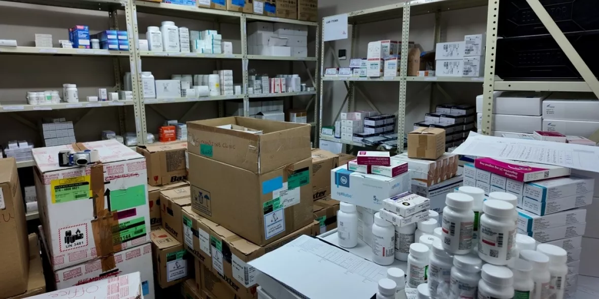 Lagerraum einer Klinik-Apotheke mit Regalen voller Medikamentenschachteln und Kartons sowie Arbeitsfläche mit Arzneiflaschen.