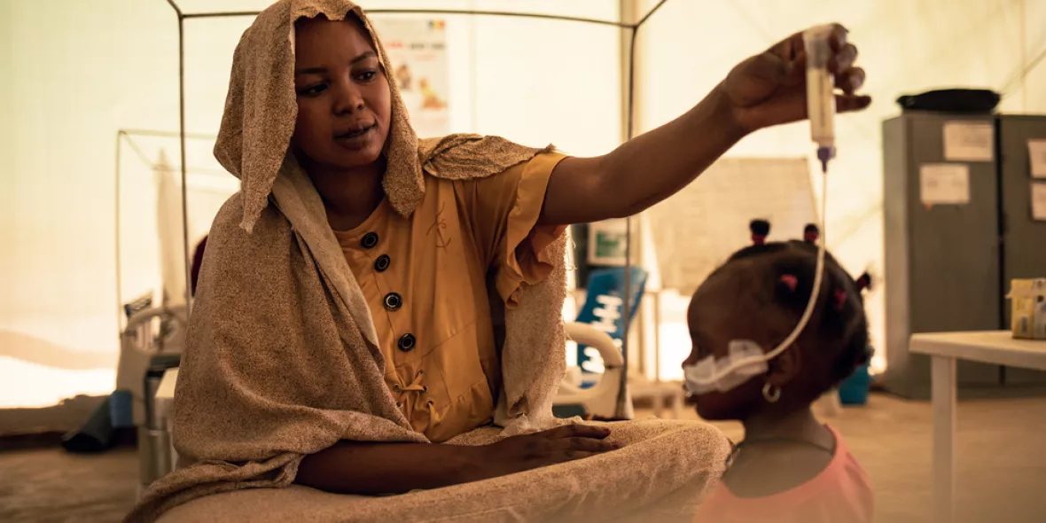 Eine Mutter sitzt auf einem Krankenbett und gibt ihrer Tochter therapeutische Milch