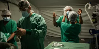 Five doctors help each other prepare their protective equipment in an operating room