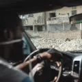 Einer unserer Mitarbeiter sitzt in einem Auto. Im Hintergrund ist die Zerstörung durch ein Erdbeben sichtbar.