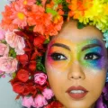 Frau mit regenbogenfarbenem Blumenkranz und Augenmakeup.