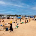 Camp aus Hütten in Wüste, dazwischen laufen Menschen