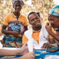 Mitarbeiter in Benin, sitzend im Gespräch mit zwei Frauen