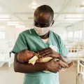Ein Krankenpfleger in Sierra Leona hält ein Neugeborenes.
