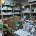 Lagerraum einer Klinik-Apotheke mit Regalen voller Medikamentenschachteln und Kartons sowie Arbeitsfläche mit Arzneiflaschen.