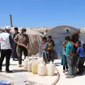 Mitarbeiter von Ärzte ohne Grenzen befüllen Wasserkanister, daneben eine Gruppe von Kindern